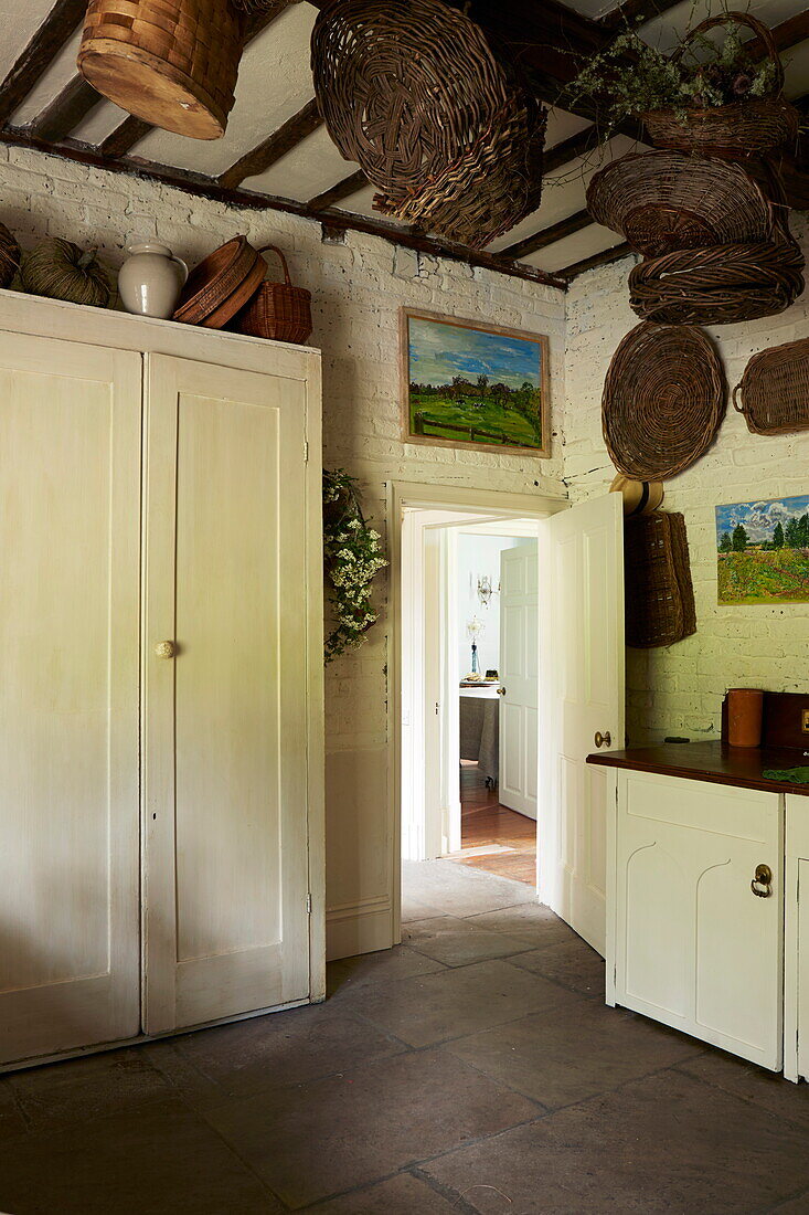 Cremefarbener Schrank und Körbe in der Balkenküche eines Hauses in Cumbria, England, UK