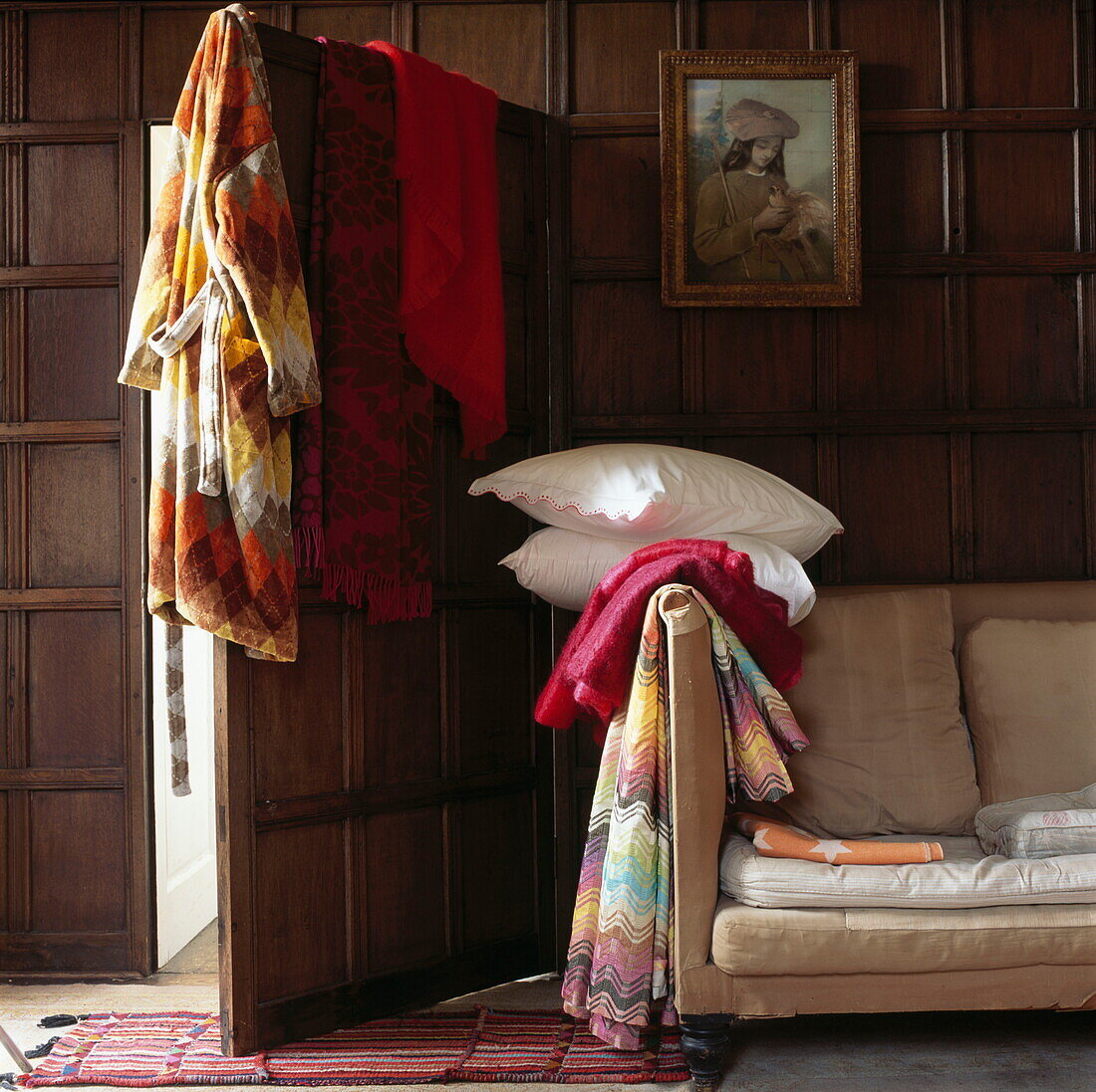 Pillows and blankets with bathrobe and sofa in panelled room of London home, UK