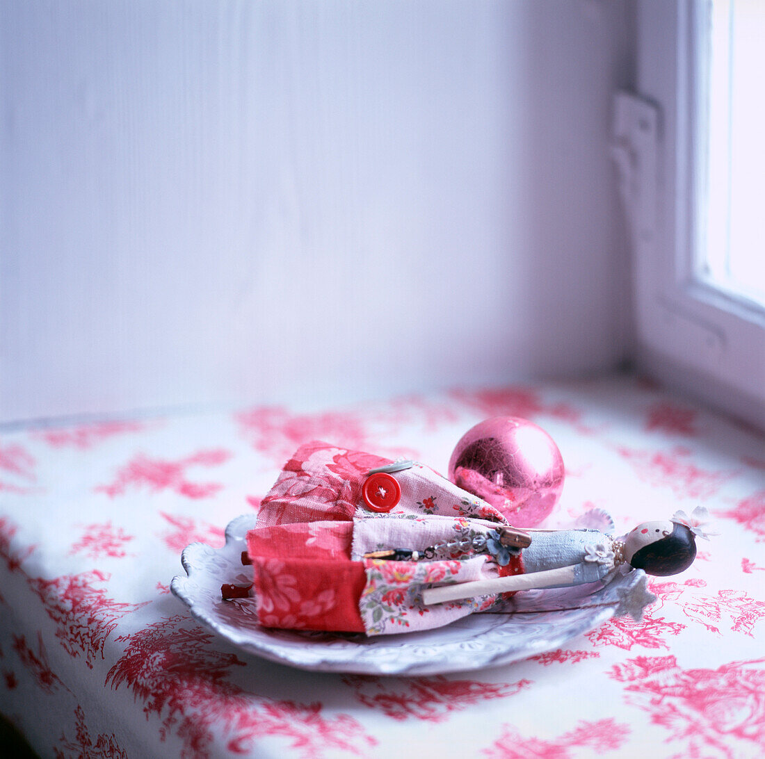Feenpuppe auf einem Teller mit einer rosa Glaskugel Rot-weiße Tischdecke
