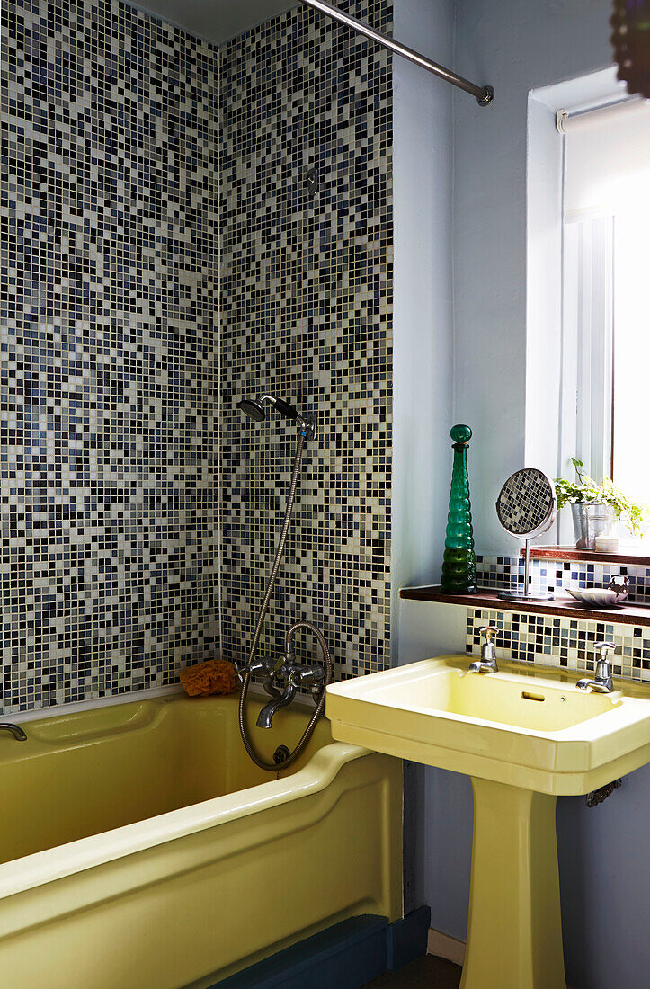 Gelbe Badewanne und Waschbecken im mosaikgefliesten Badezimmer einer Wohnung in Hackney, East London, UK