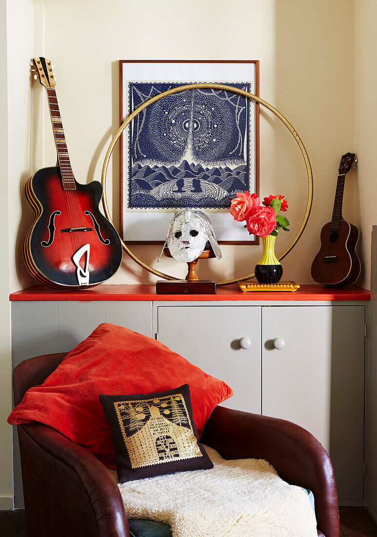 Gitarre und Ukulele mit Hula-Hoop-Reifen auf Schrank mit braunem Ledersessel im Wohnzimmer in Hackney, East London, UK