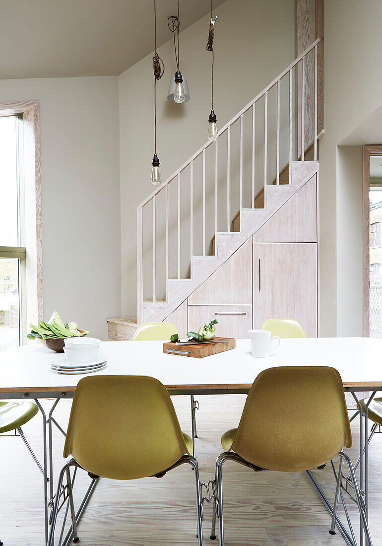 Dining room table with lime green chairs and staircase in contemporary London home, England, UK