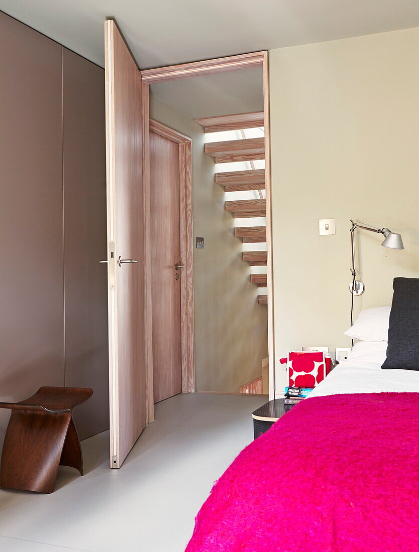 Leuchtend rosa Bettdecke mit Holzhocker und Blick durch die Tür in einem modernen Haus in London, England, Vereinigtes Königreich