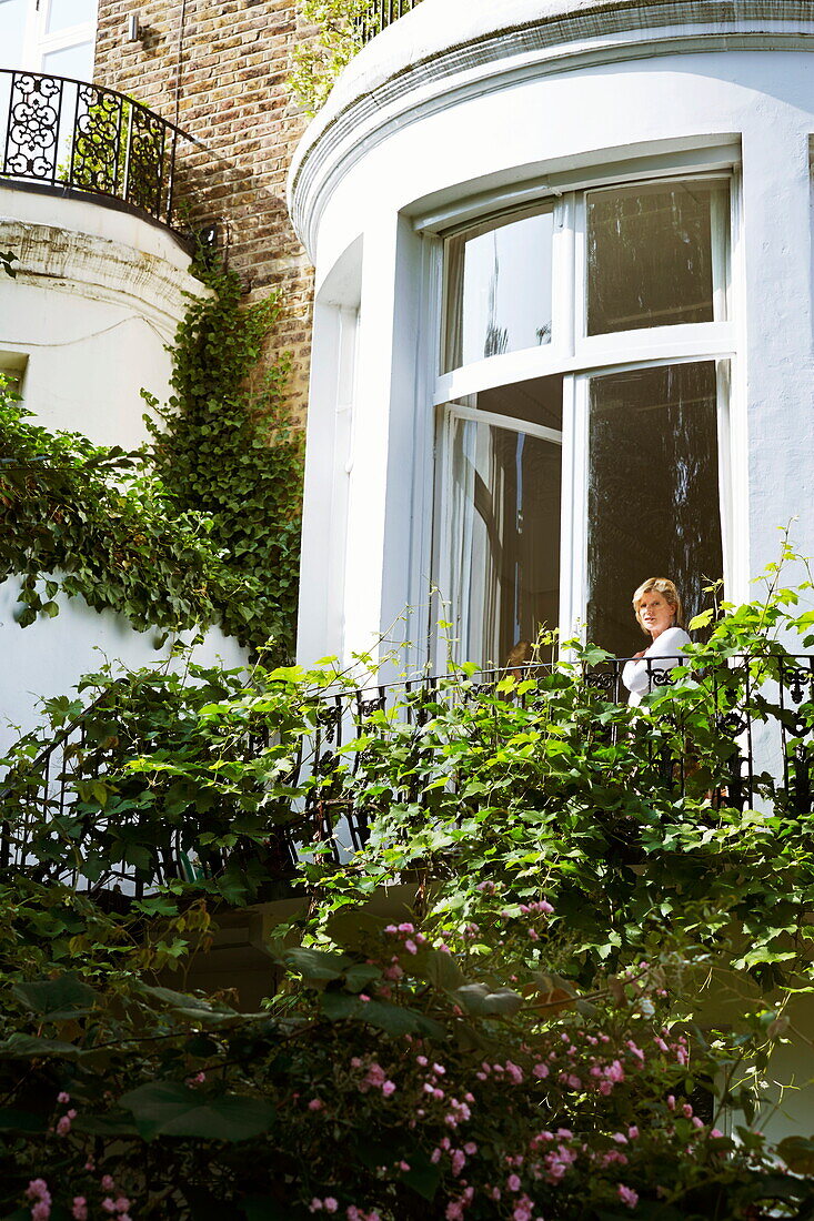 Frau steht in einem geschwungenen Erkerfenster eines Londoner Stadthauses, England, Vereinigtes Königreich
