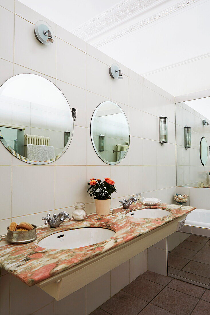 Doppelwaschbecken mit runden Spiegeln im gefliesten Badezimmer eines Stadthauses in London, England, UK