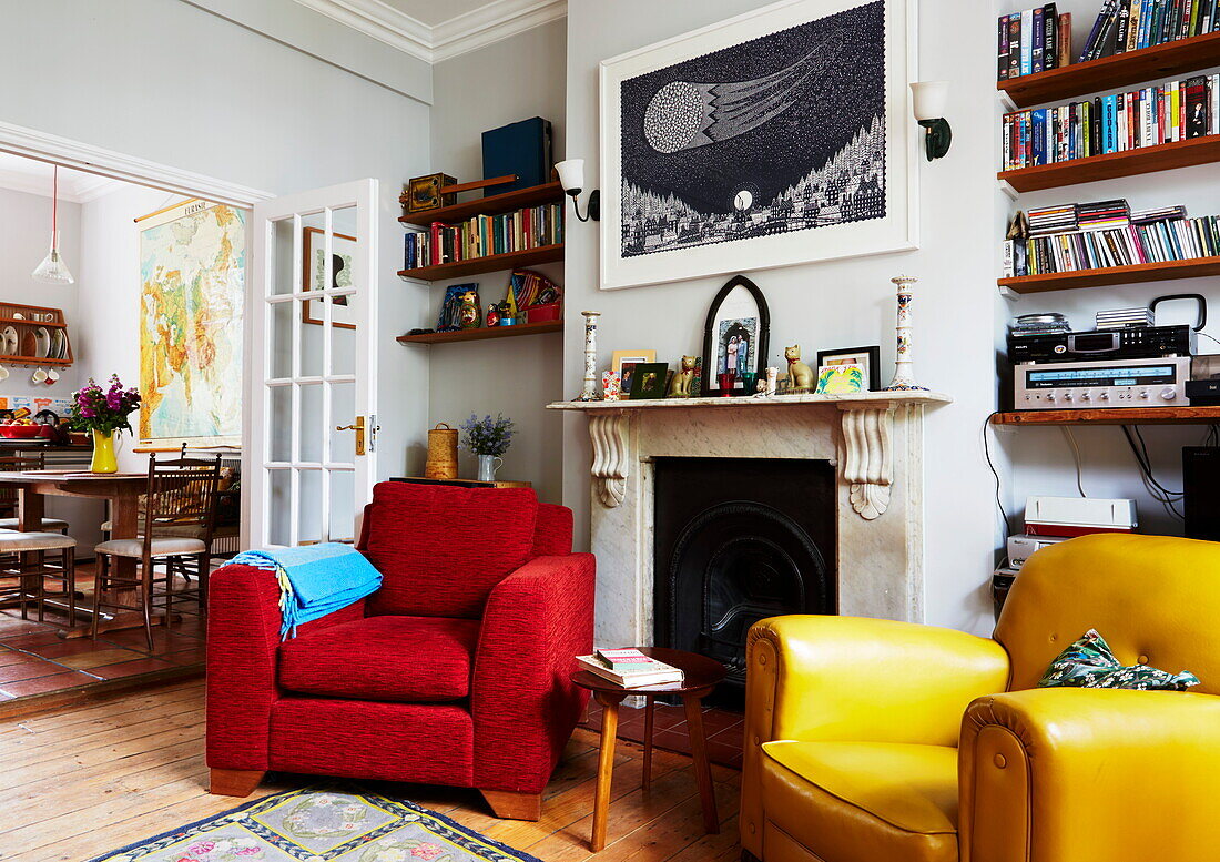 Red and yellow armchairs at fireside in living room of colourful London home, England, UK