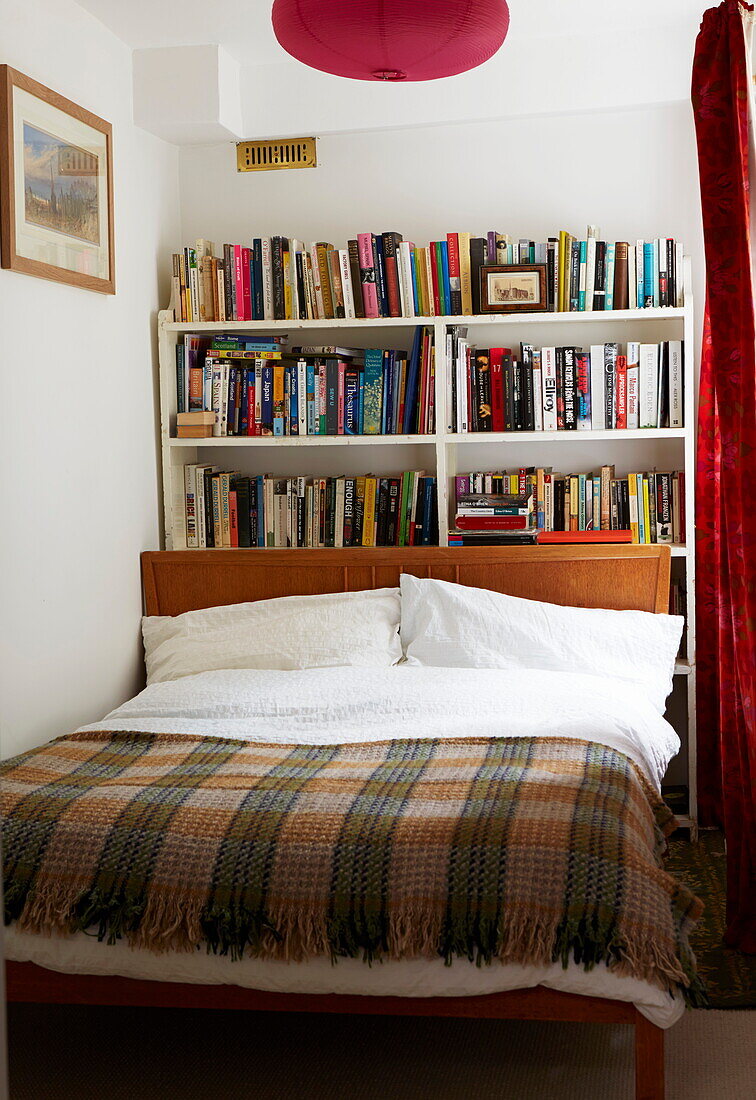Checked blanket on double bed with books in London home, England, UK