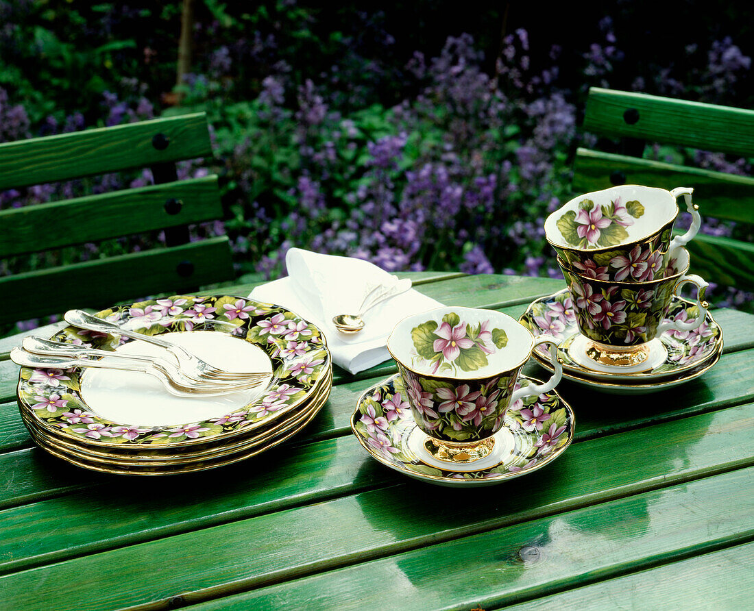 Tassen, Untertassen und Teller mit Blumenmuster auf einem grün gestrichenen Gartentisch