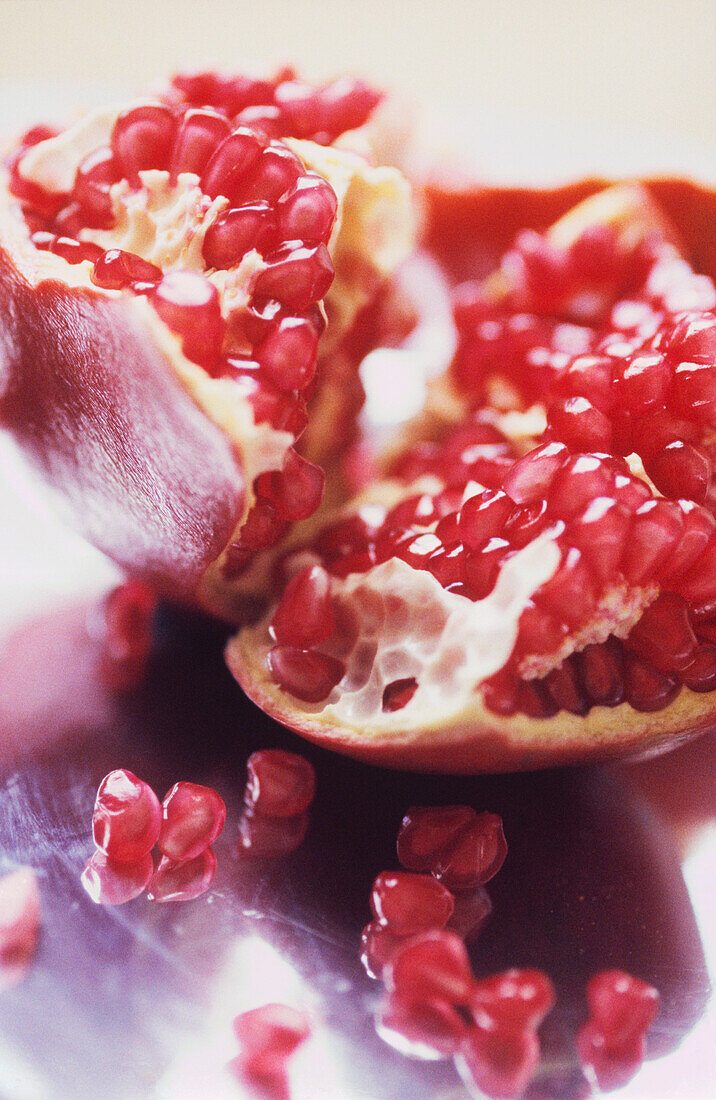 Ripe pomegranate torn open to reveal red seeds on a shiny metal background