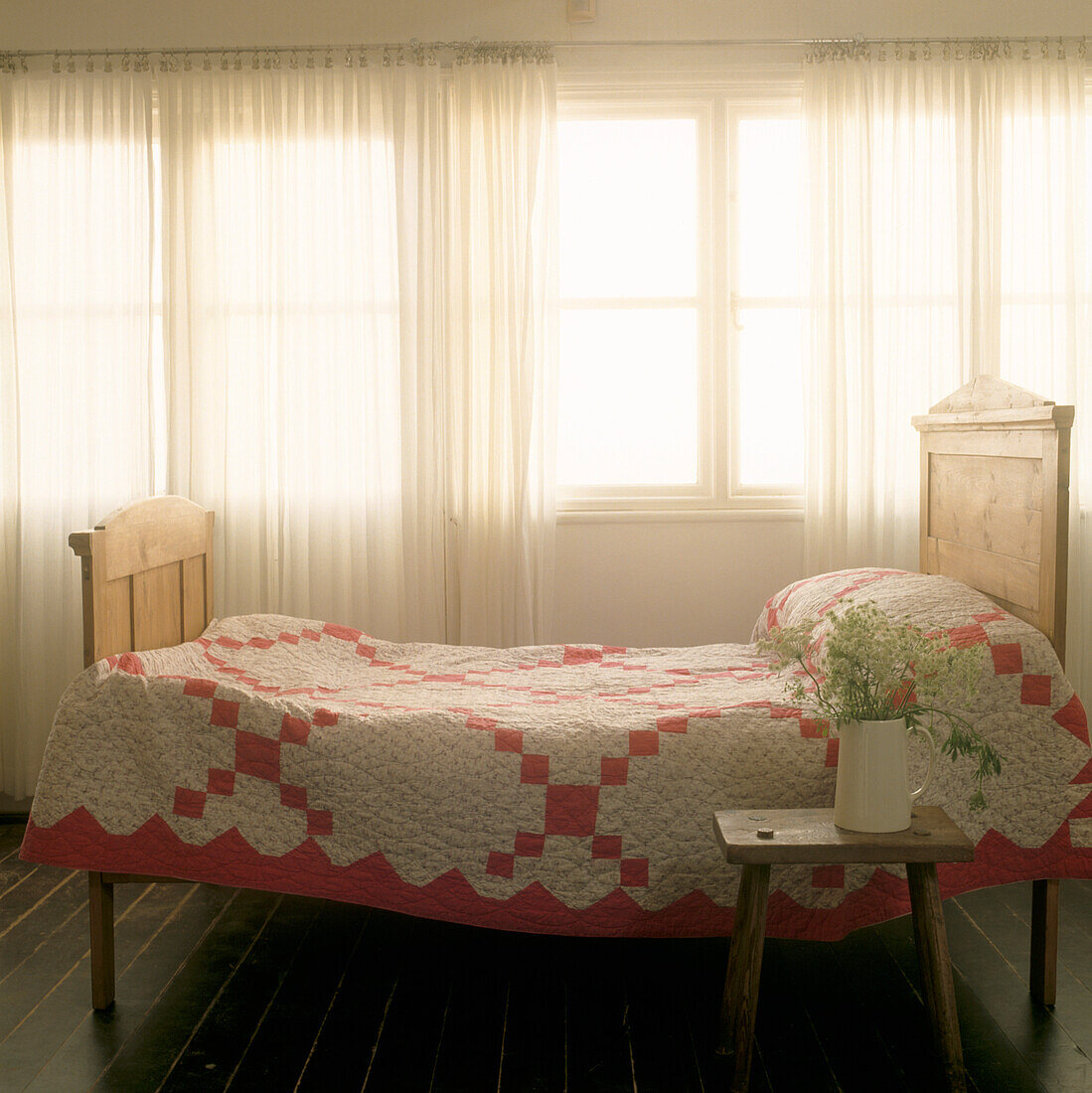 Fensterbild mit Einzelbett aus Kiefernholz und rot-weißer Bettdecke