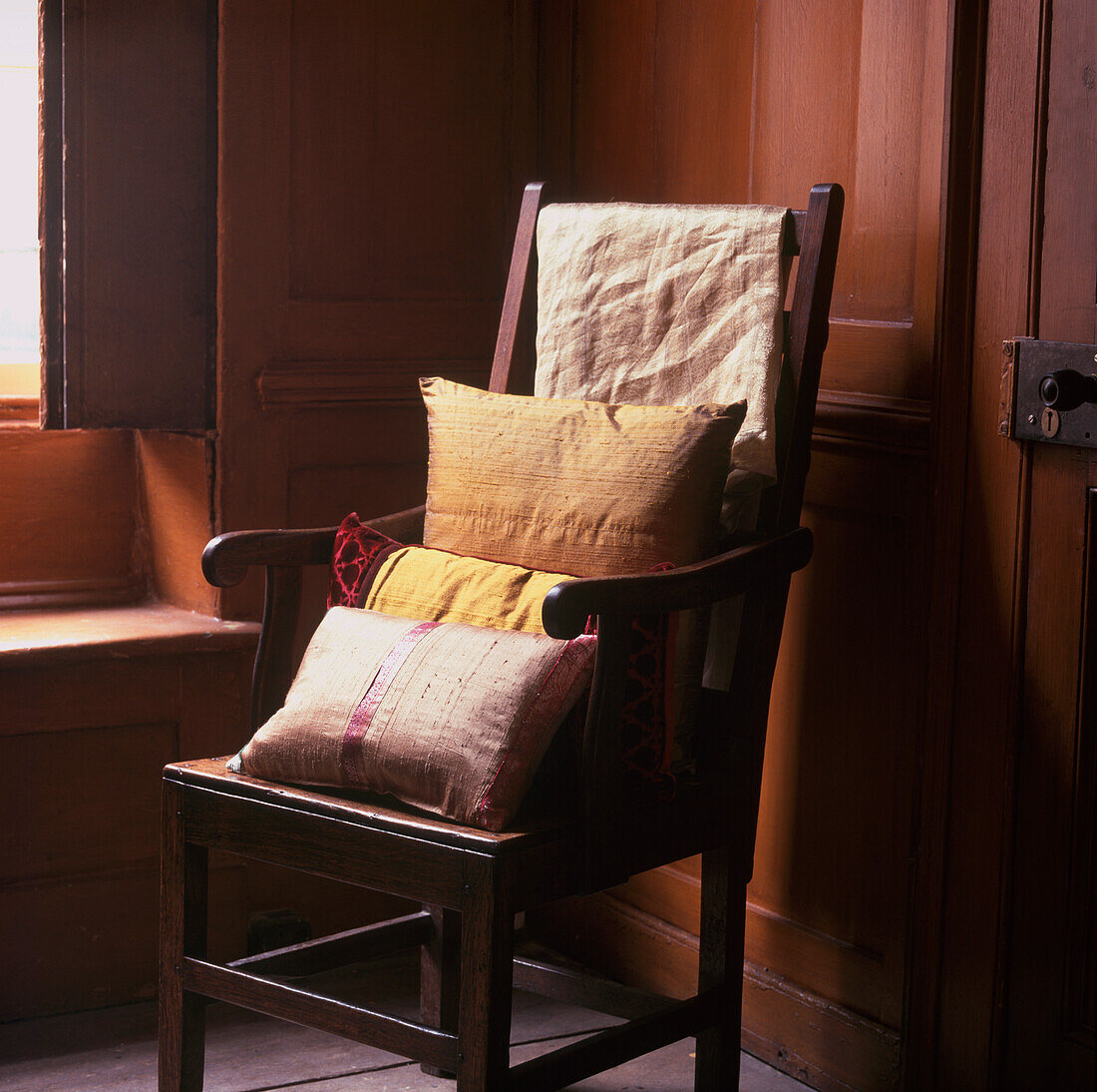 Seidenkissen auf einem Hochlehner-Sessel in einem dunkel getäfelten Raum