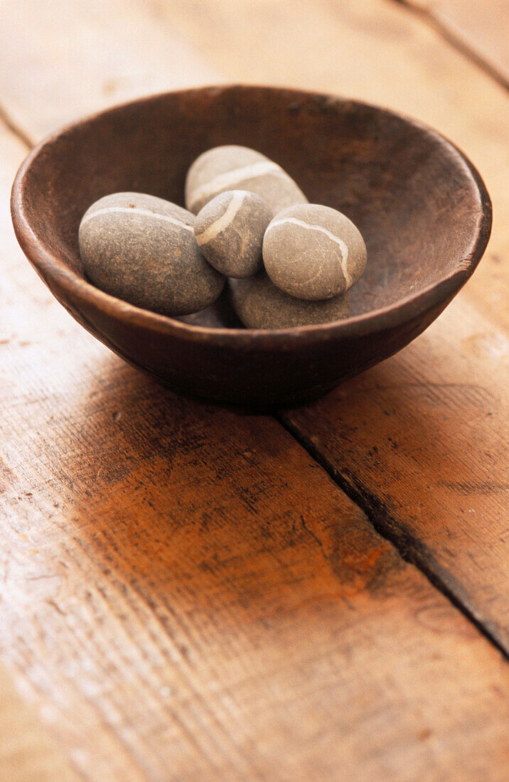 Holzschale mit grauen und weißen Steinen auf Tischplatte