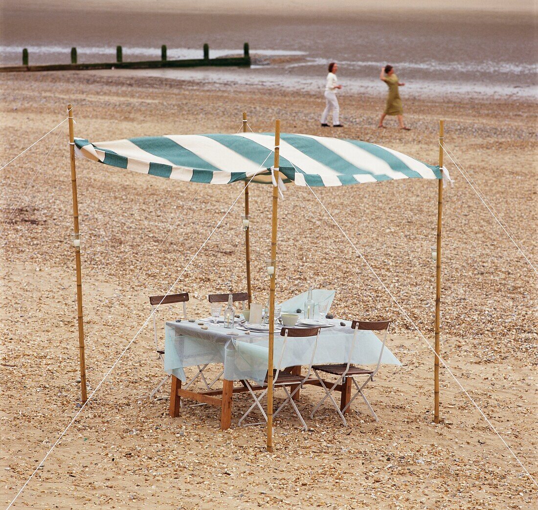 Tisch und Stühle am Strand unter einem gestreiften Baldachin