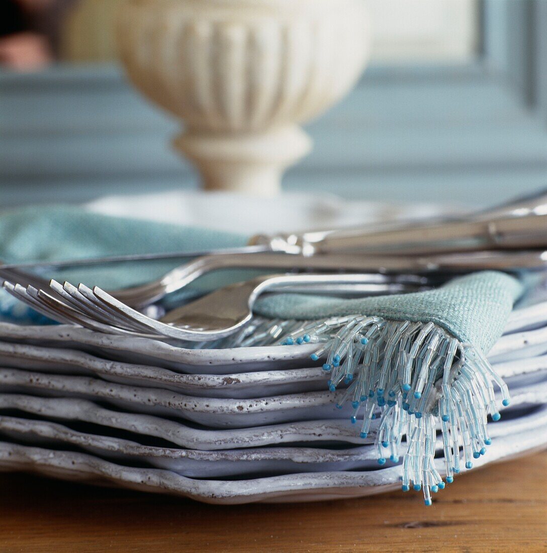 Silver forks on stack of plates with fringed fabric