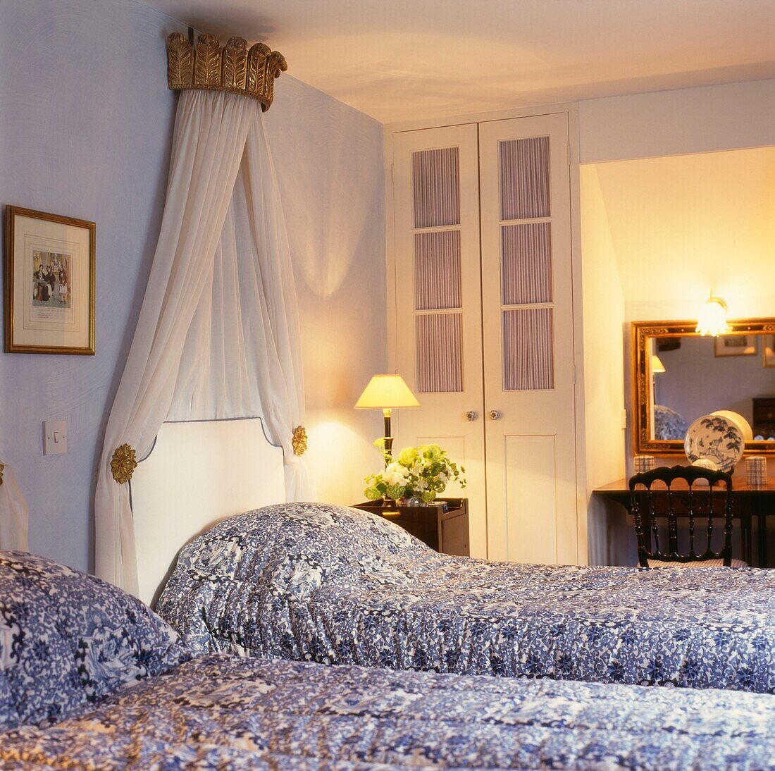 Twin beds with canopy and lit lamps in pastel blue bedroom 