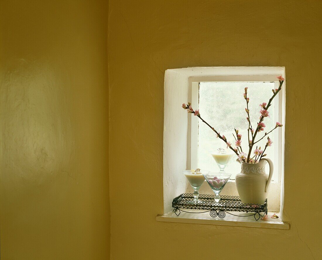 Krug mit Frühlingszweigen auf einem quadratischen Fenster in einem gelb gestrichenen Zimmer