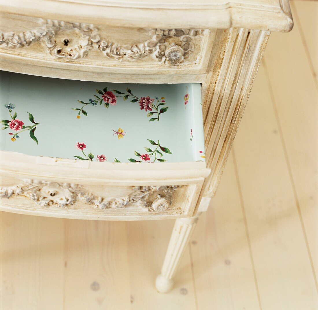 Open drawer on chest lined with floral wallpaper