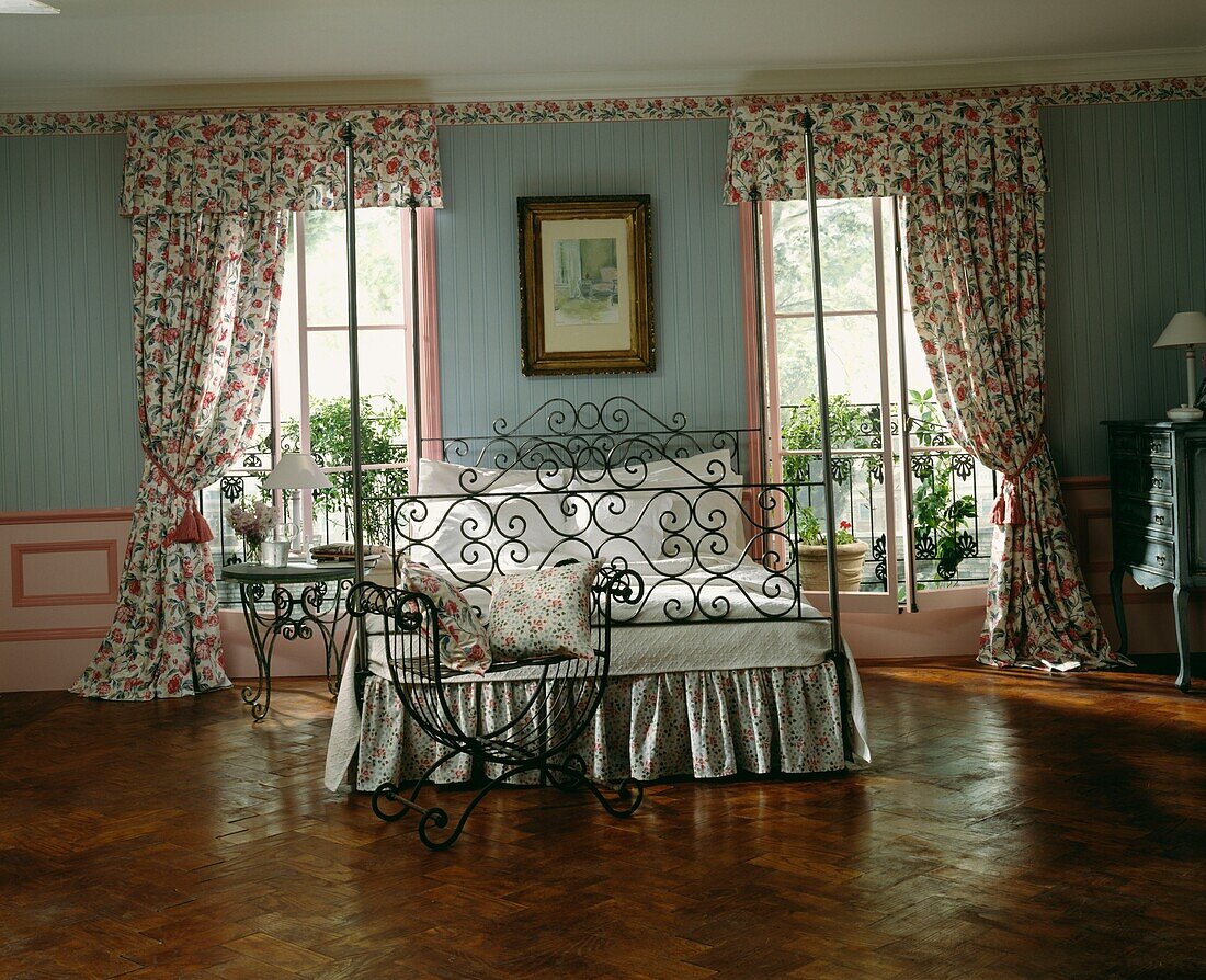 Wrought iron bed at windows with co-ordinated floral print curtains and pelmets