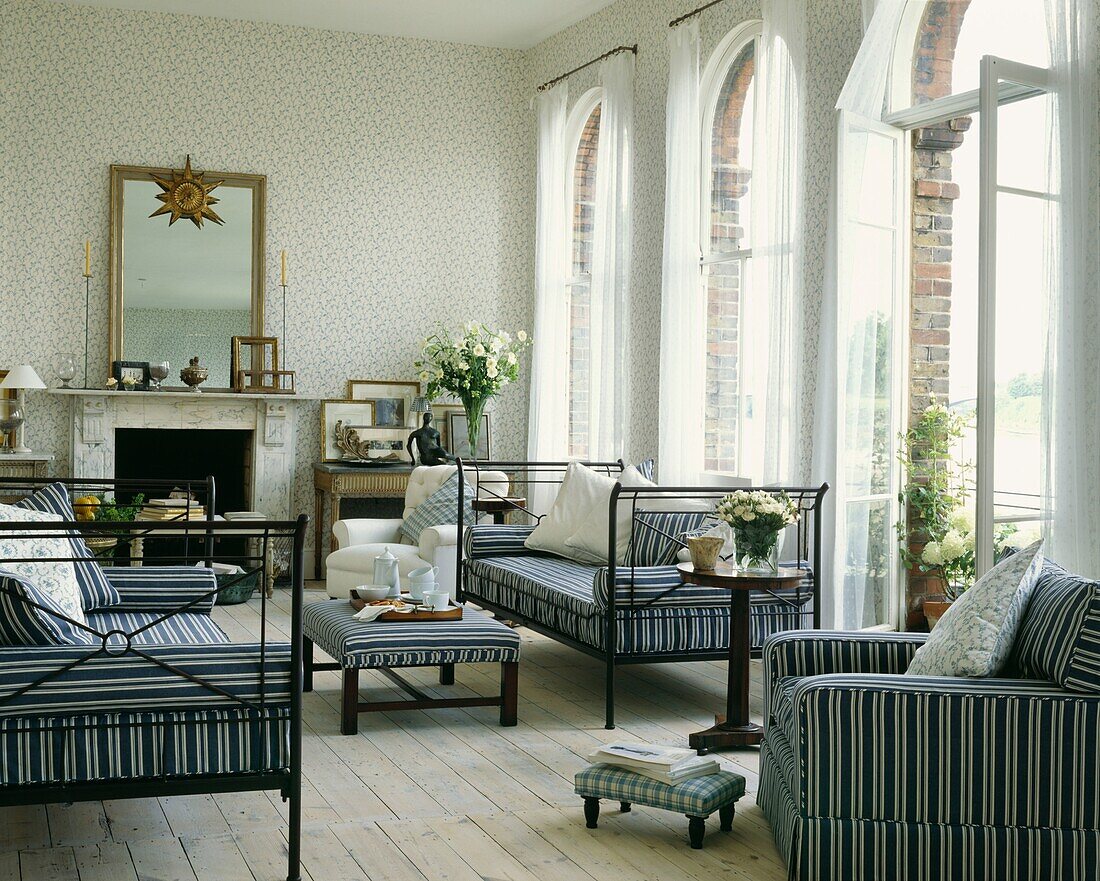 Gestreifte Polsterung passend zu den Möbeln im Wohnzimmer mit gestrichenen Dielen und hohen Bogenfenstern