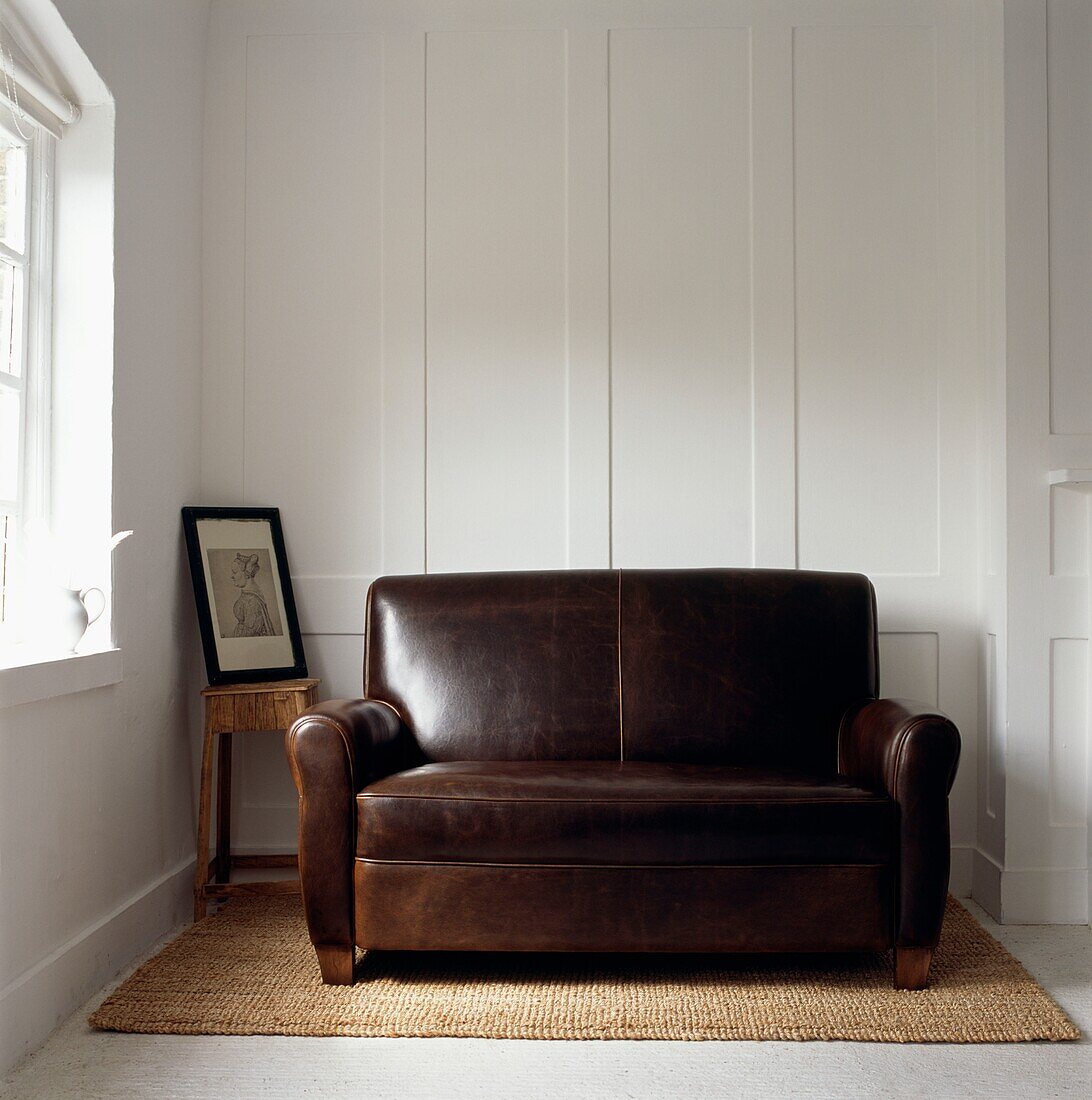 Brown leather two-seater sofa on seagrass rug with white panelled wall