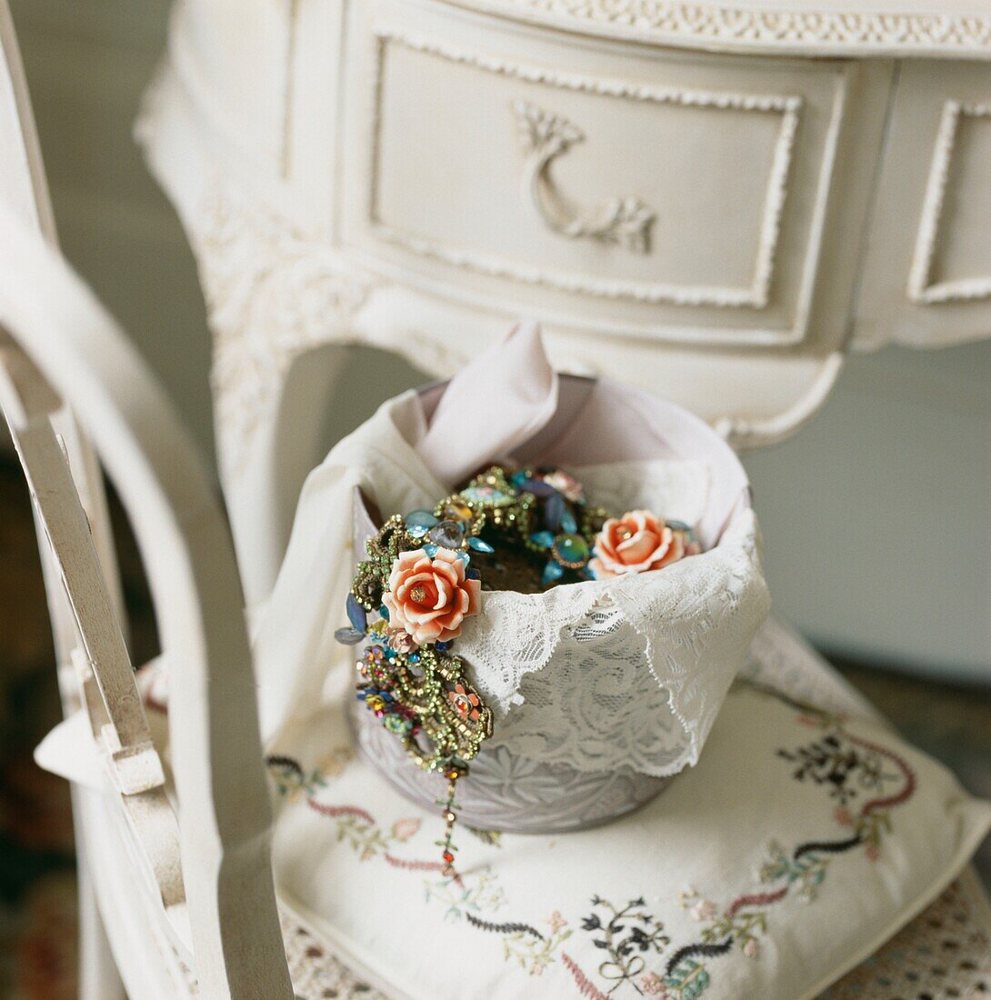 Rosenschmuck in Porzellanschale mit Spitze auf Stuhl mit gesticktem Kissen