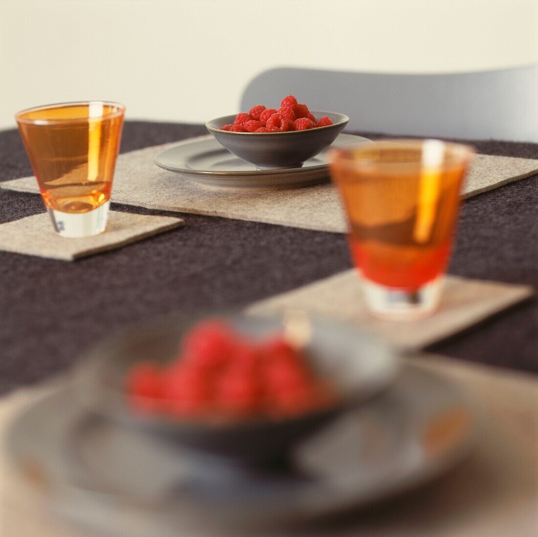 Schalen mit Himbeeren und buntem Glas auf einem Esstisch mit strukturiertem Stoff