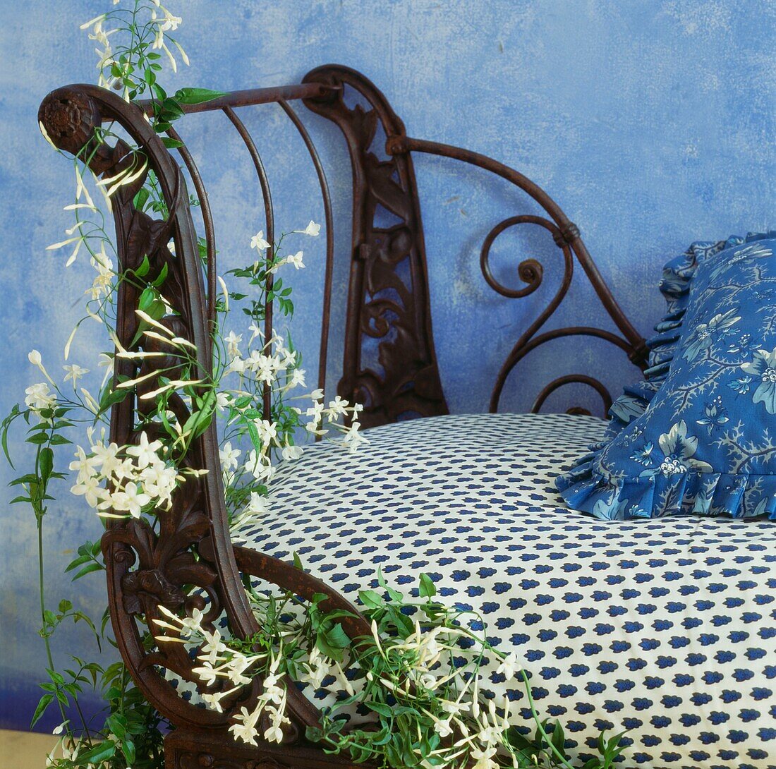 Ornate metalwork bench with cushions and jasmine