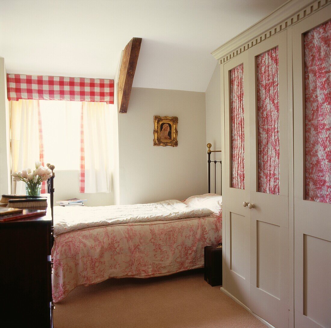 Einzelbett in einem Zimmer mit gemusterten Schränken mit Glasfronten und sonnendurchflutetem Fenster