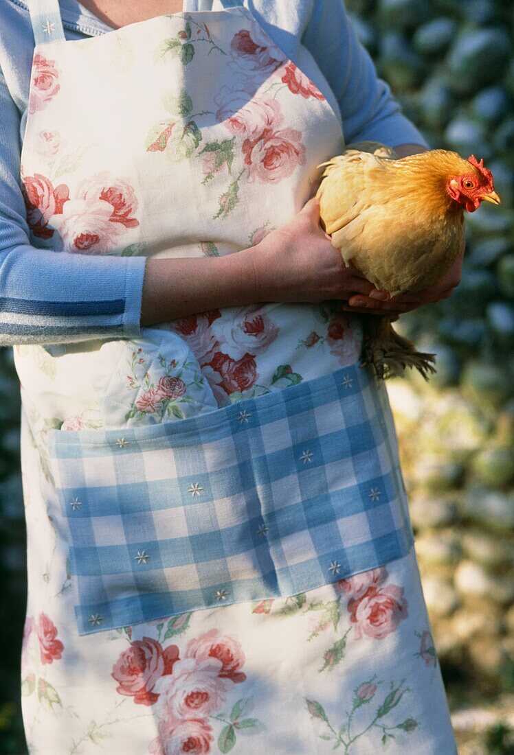 Frau in Schürze, die ein Huhn hält