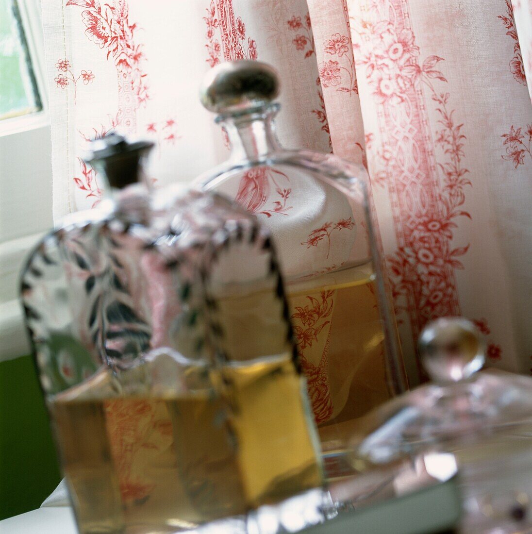 Parfümflaschen auf der Fensterbank mit blumengemusterten Vorhängen