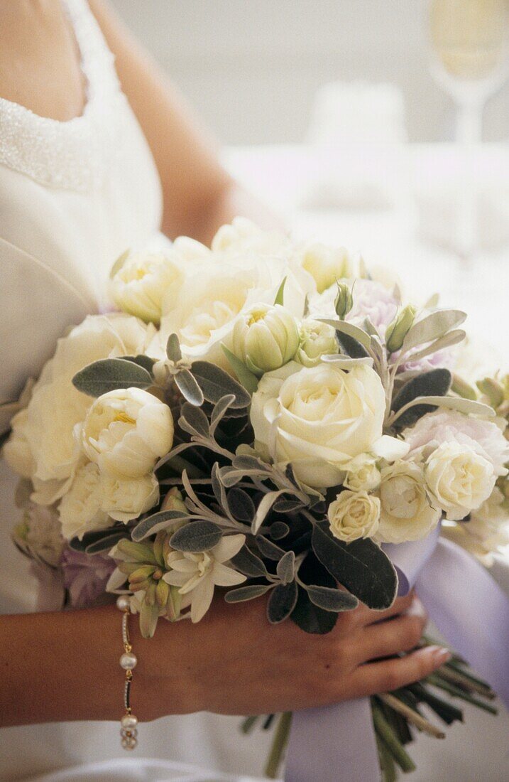 Die Braut hält einen Brautstrauß aus weißen Blumen und silbergrünen Stachys