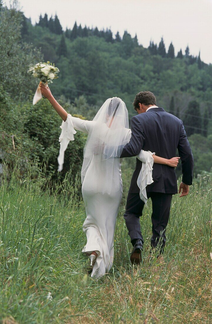 Braut und Bräutigam gehen über ein Feld in der italienischen Landschaft