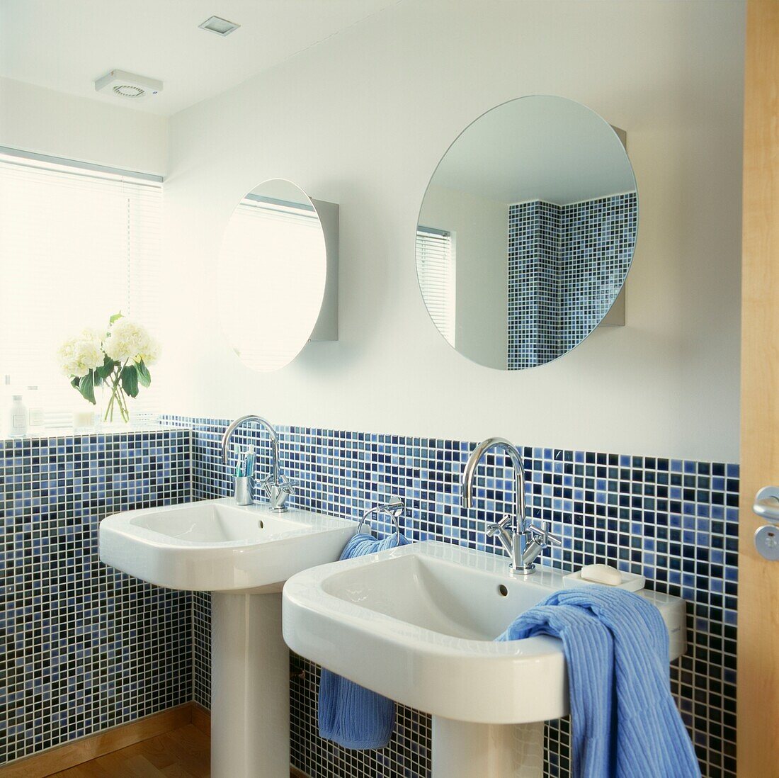 Doppelwaschbecken in einem sonnenbeschienenen, mosaikgefliesten Badezimmer mit runden Spiegeln
