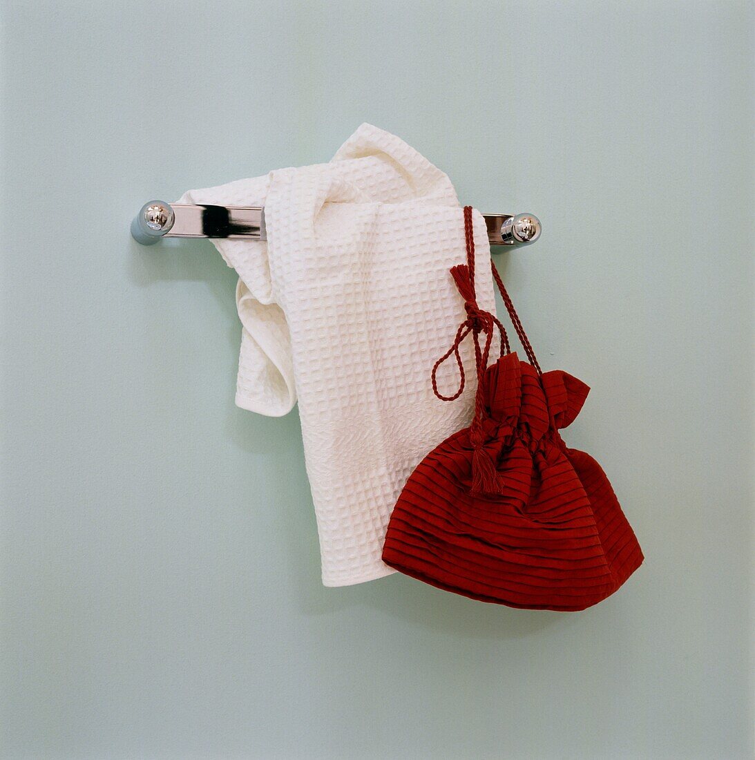 Red bag and white towel hang on bathroom wall