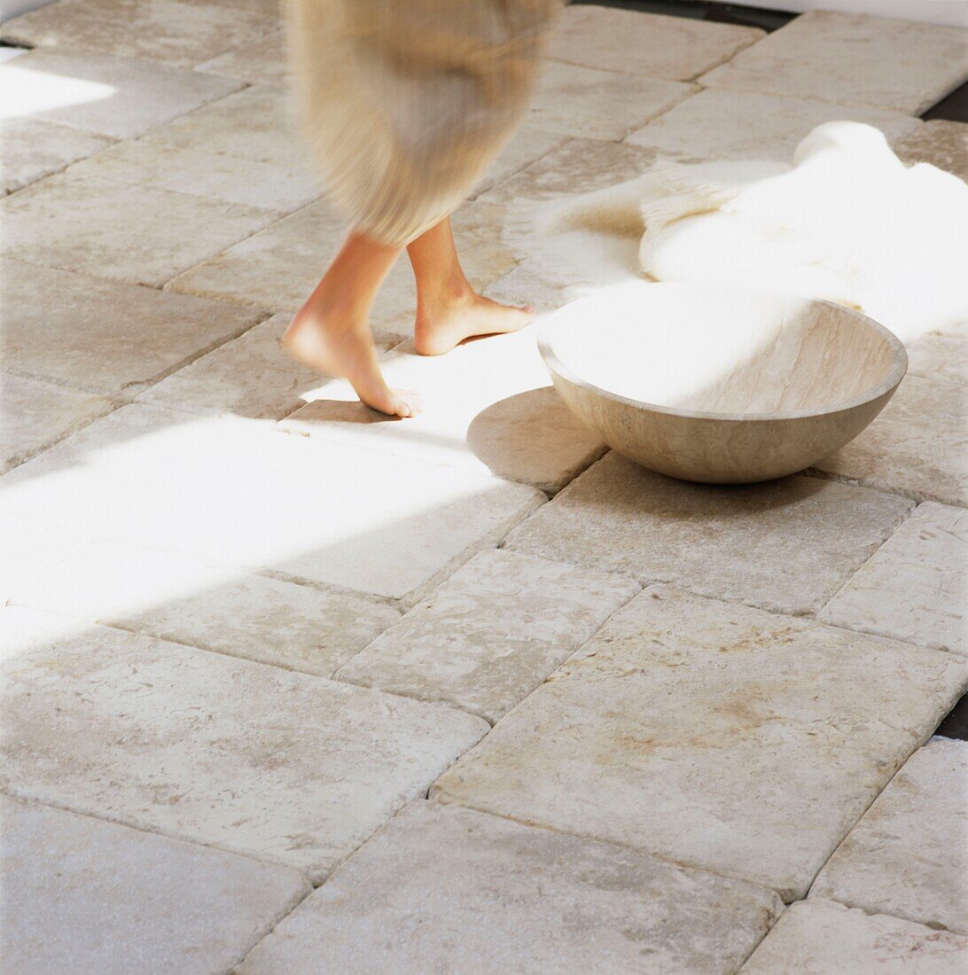 Niedriger Ausschnitt einer Frau, die mit einer Waschschüssel über einen Steinboden geht