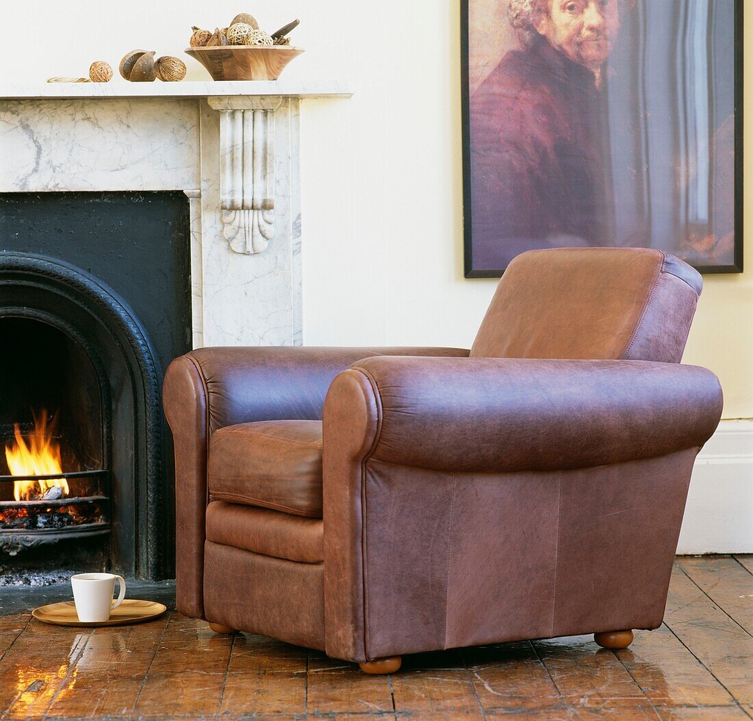 Leather armchair beside marble fireplace with mug and oak floorboards