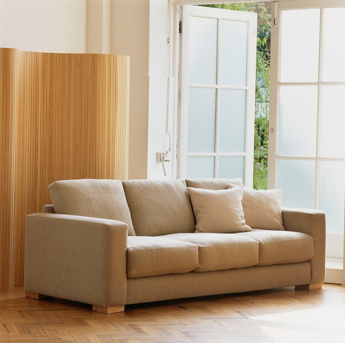 Beige upholstered sofa in living room beside and open door and wooden screen