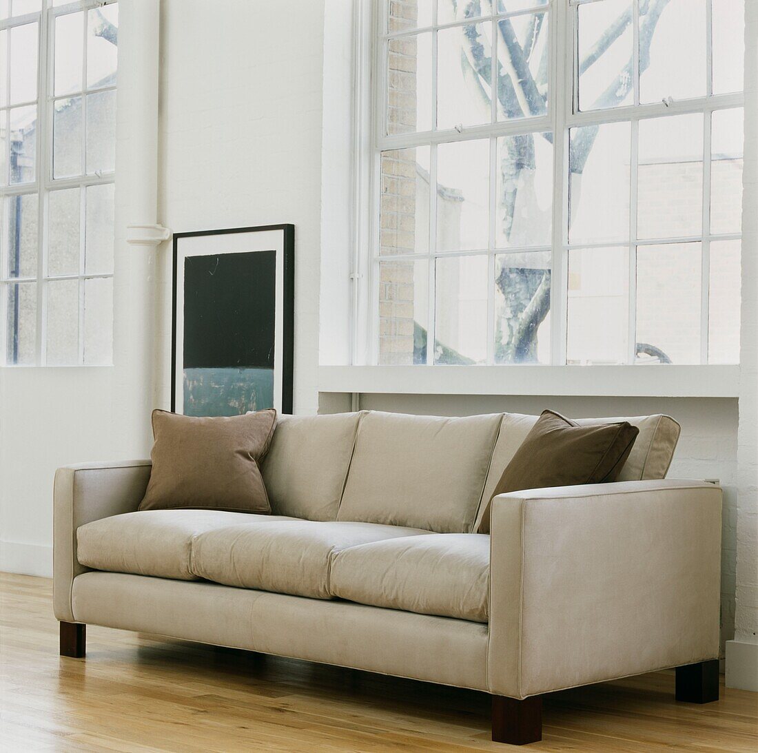 Cremefarbenes Sofa mit modernem Kunstwerk an einem Fenster ohne Vorhang