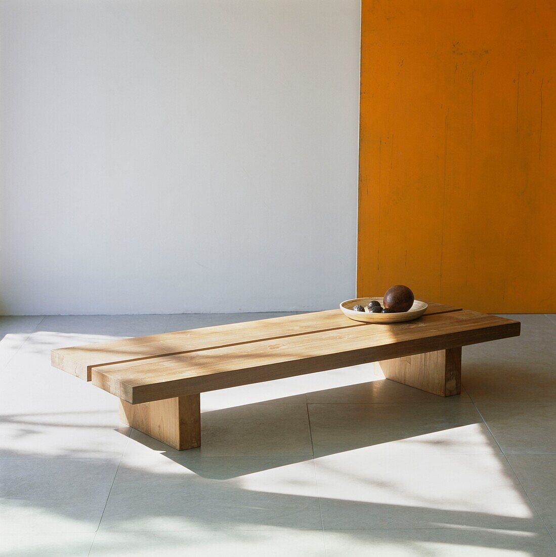 Klobiger Holzcouchtisch mit Holzschale auf Steinfliesenboden mit orangefarbener Wand