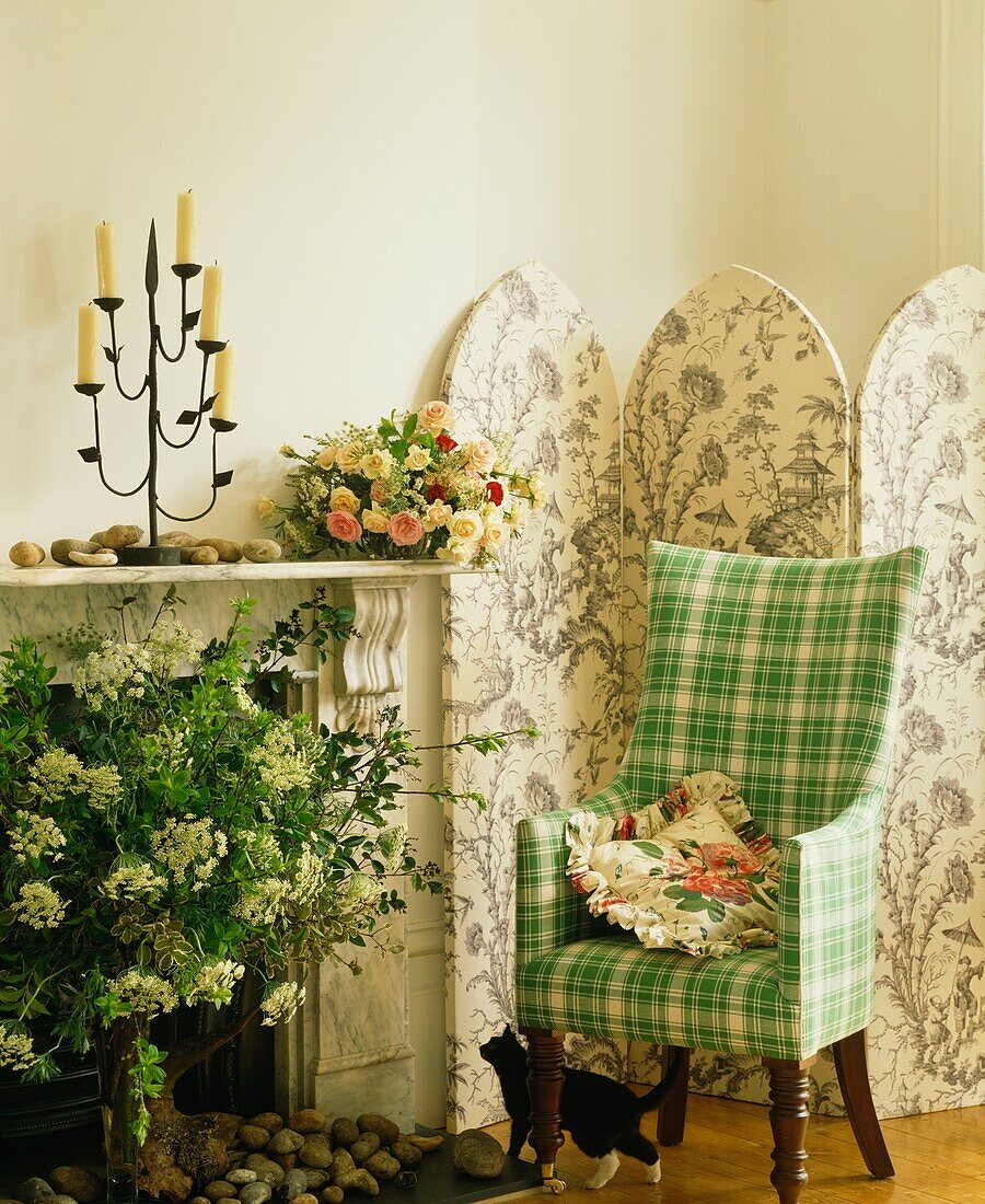Checked green armchair with flower arrangement and folding screen at marble fireplace