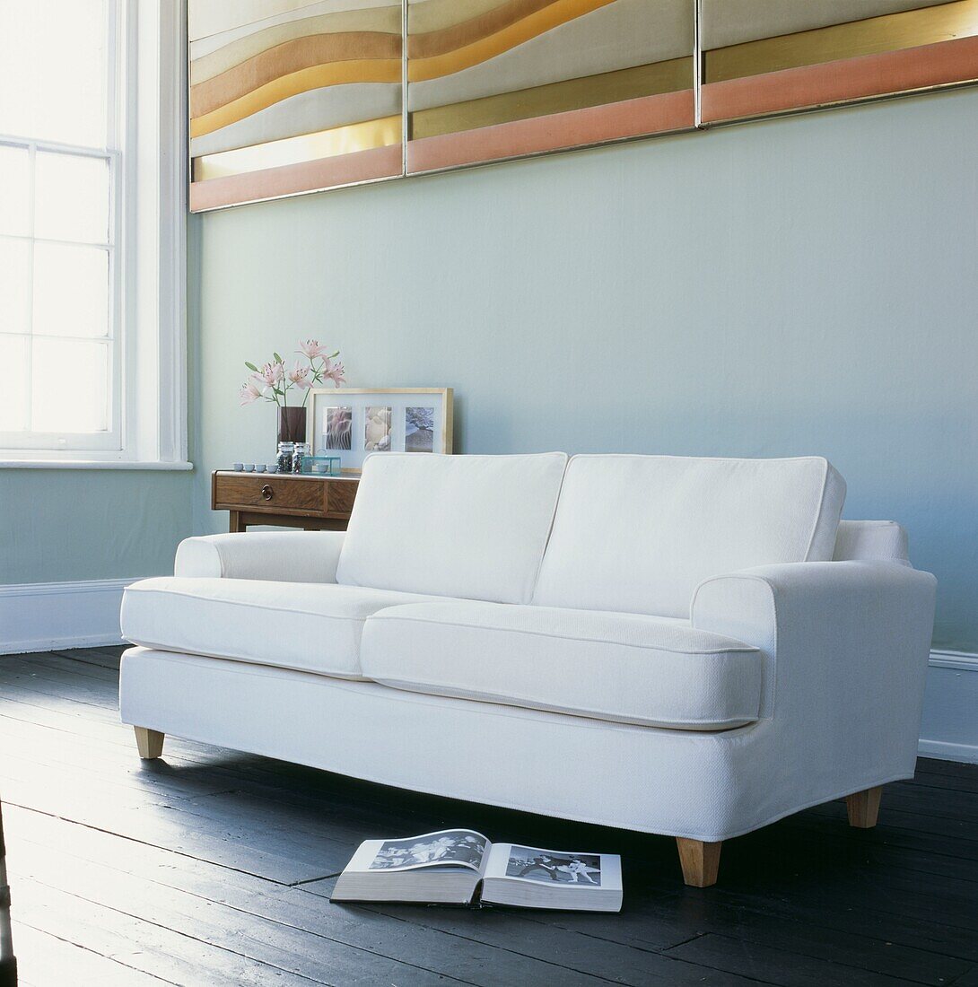 Weißes Sofa in einem Raum mit moderner Kunst und offenem Buch auf Dielen