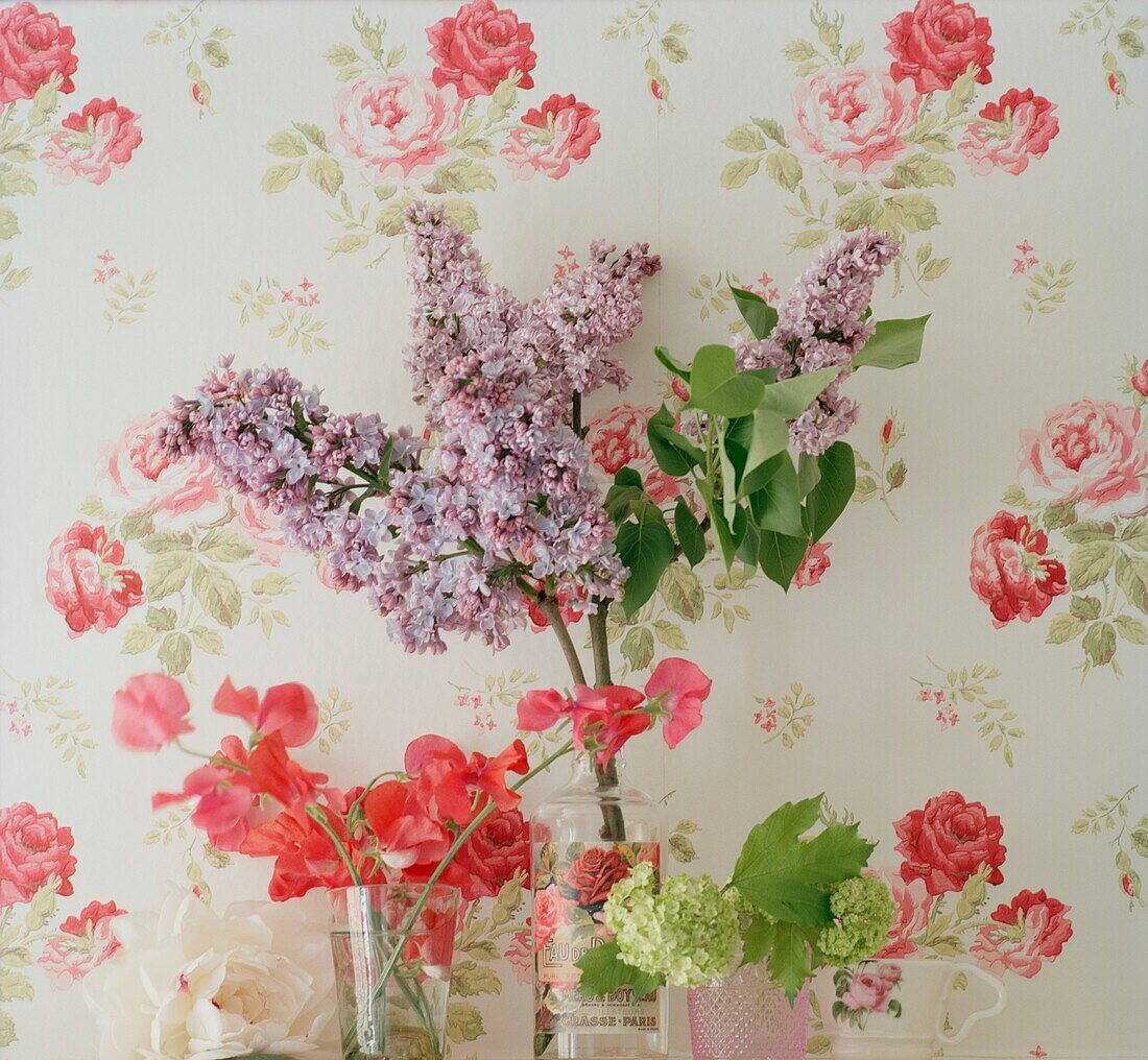 Cut summer flowers set against floral patterned wallpaper