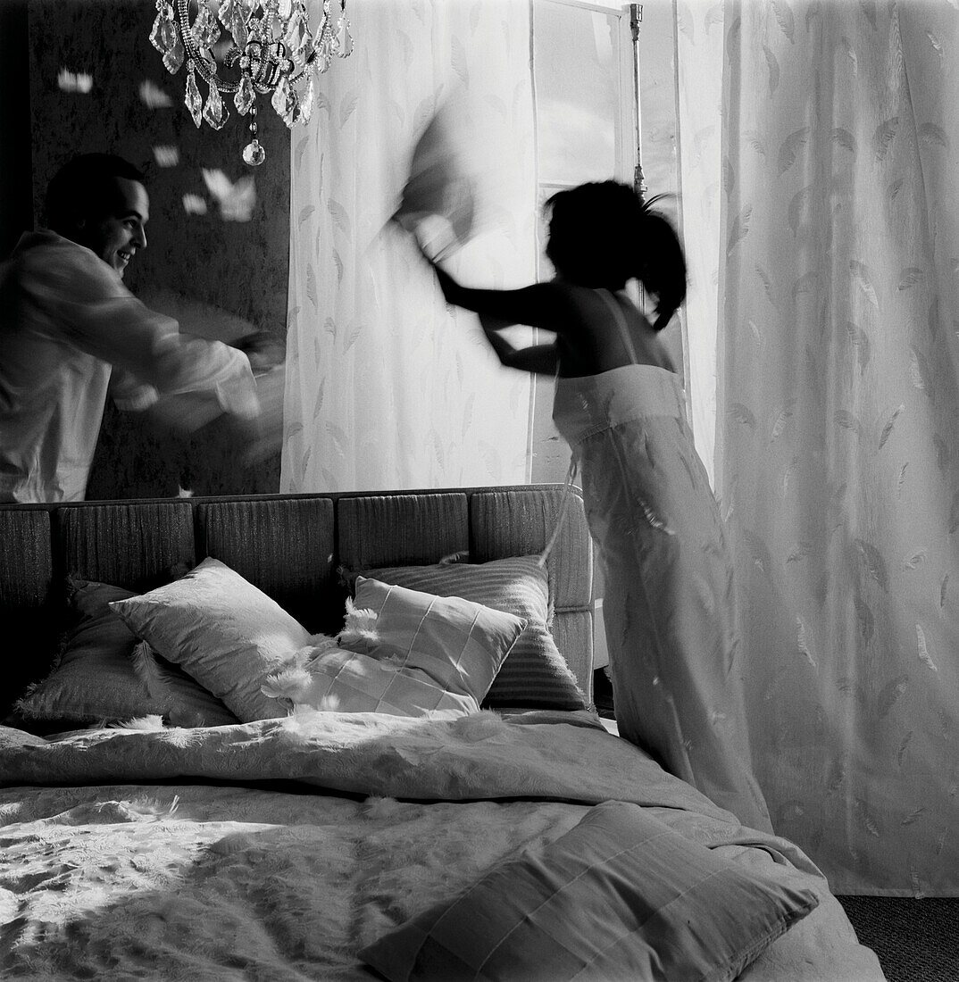 Couple have a pillow fight on a bed in a bedroom