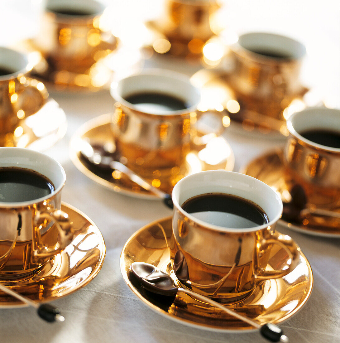 Goldene Tassen mit gewürztem Kaffee und in dunkle Schokolade getauchte Löffel