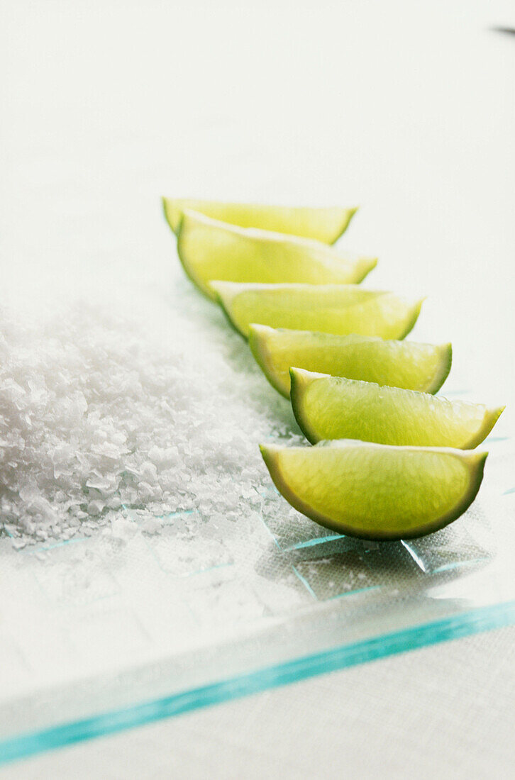 Geschnittene Limettenspalten auf einem Glasbrett mit Meersalz zur Zubereitung eines Margarita-Cocktails