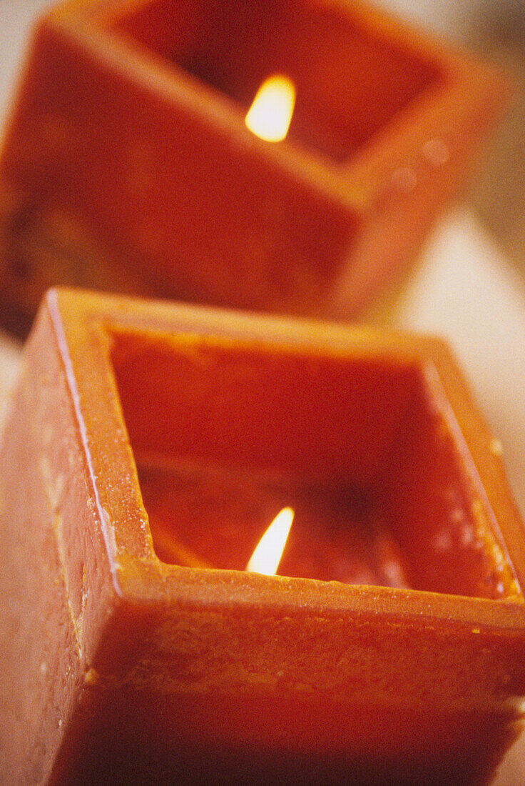 Close up of two square shaped orange wax candles