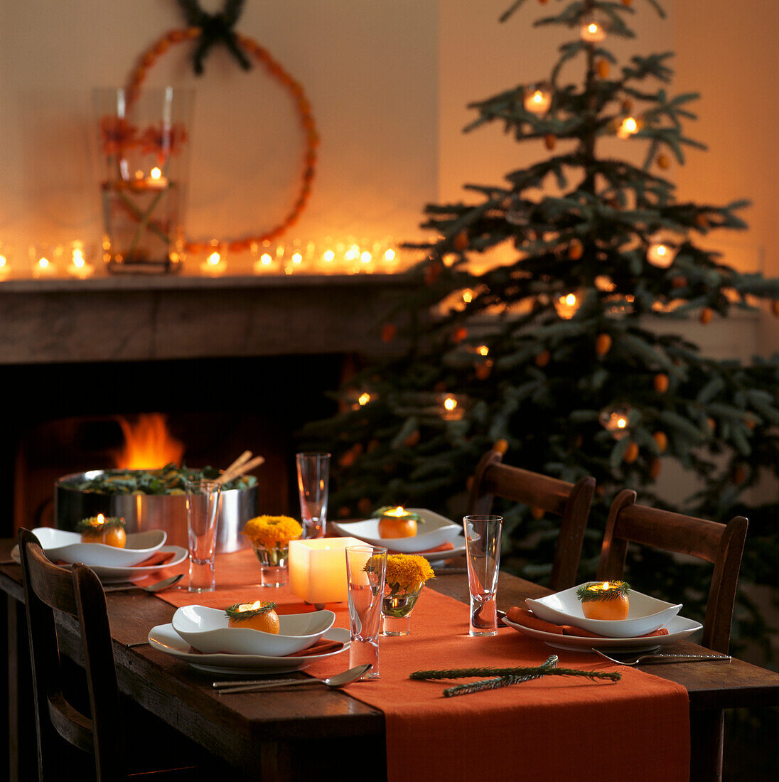 Weihnachtlich gedeckter Tisch in Orangetönen mit offenem Feuer und flackernden Kerzen