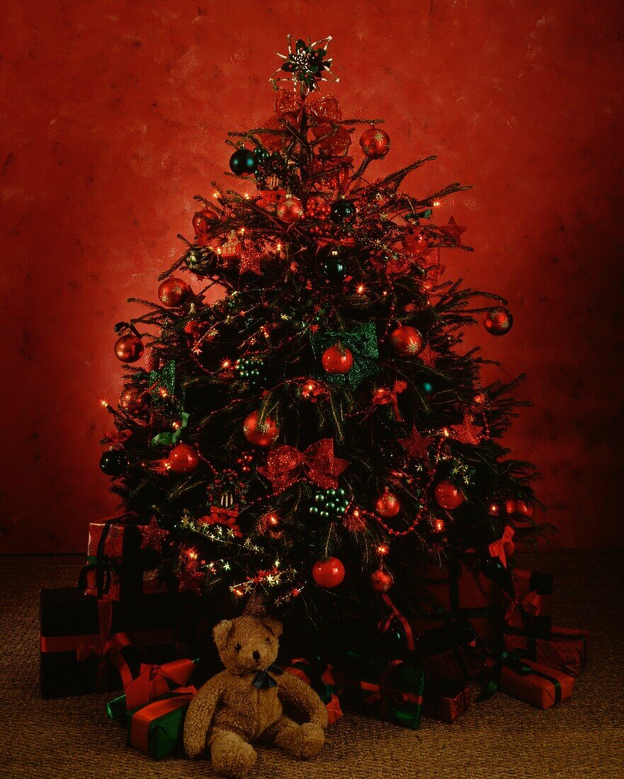 Teddy bear and wrapped gifts under Christmas tree decorated in red