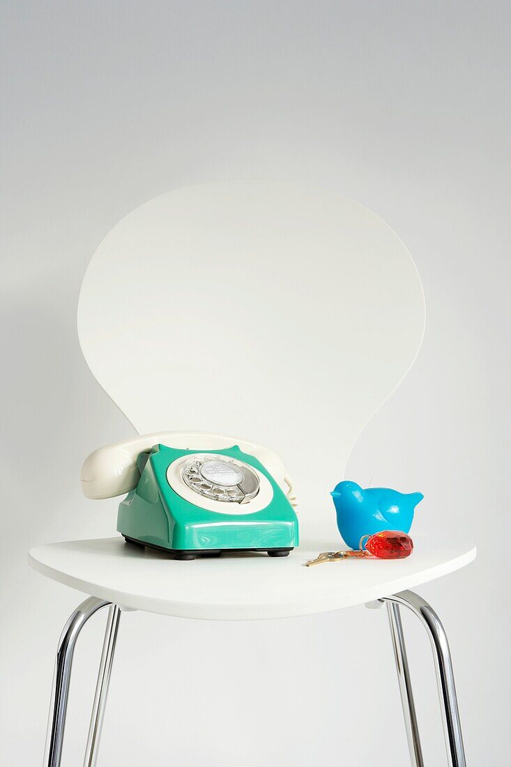 Grünes Vintage-Telefon auf weißem Stuhl mit Plastik-Vogelspielzeug und Schlüsselanhänger