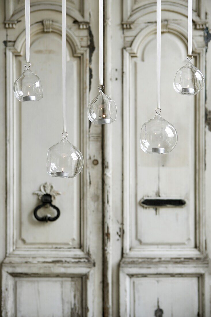 An Bändern hängende Glaskugeln mit funkelnden Teelichtern vor einer alten, verzierten, getäfelten Eingangstür